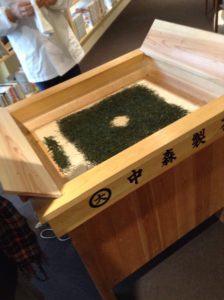 手揉み茶の乾燥。真ん中に穴をあけます。左手の小さな塊は細かいお茶を集めてます。