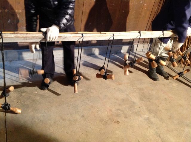 [2]まずデモで、よしずづくりのプロの実演を見せていただきました。 ヨシを一本、木の上にのせます。そのあと、重しのついた縄を交差させます。 最初の一本の写真。縄が全部の箇所でくくられていく途中です。 黒い縄のさきに結びつけられている木は重しです。 重しの重さは300-400gだと思います。 重しの重さだけで縄が締まっていきます。